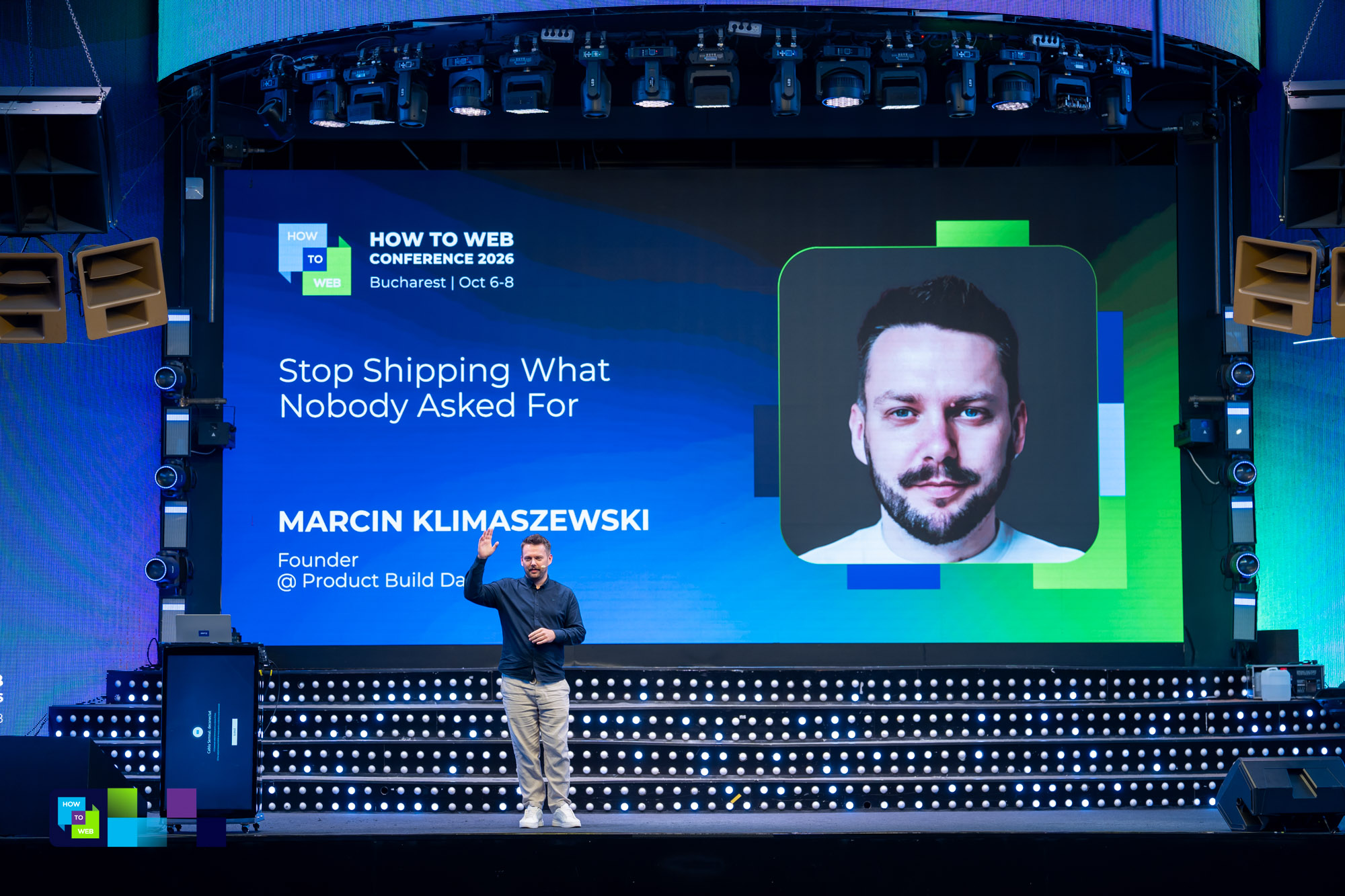 Marcin waving on the main stage at How to Web, with the session title and his speaker card on the big screen