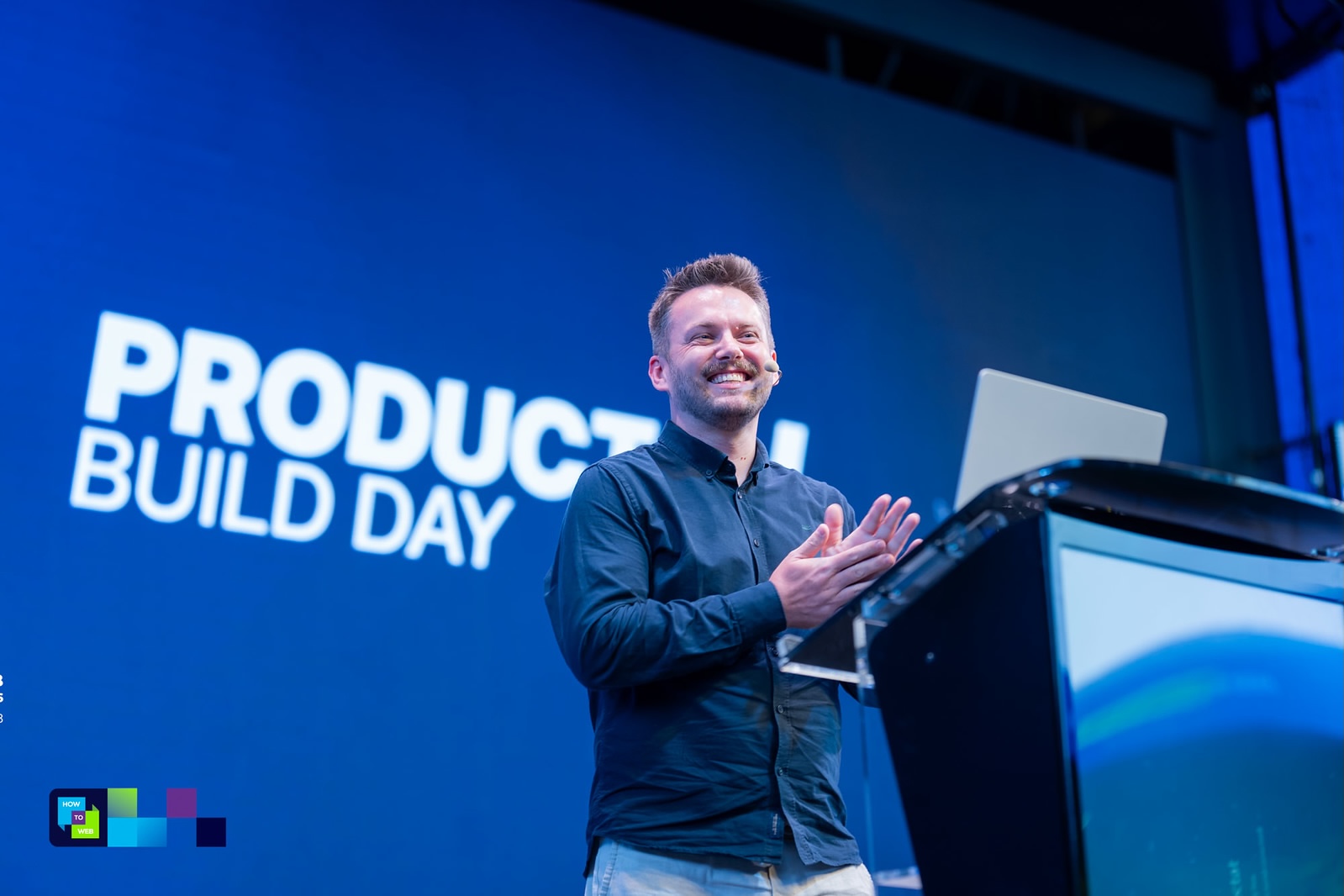 Marcin on the How to Web main stage, mid-session, with the Product Build Day screen behind him